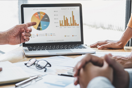 Hands shown around a laptop with a graph on the screen. One hand is pointing at the screen.